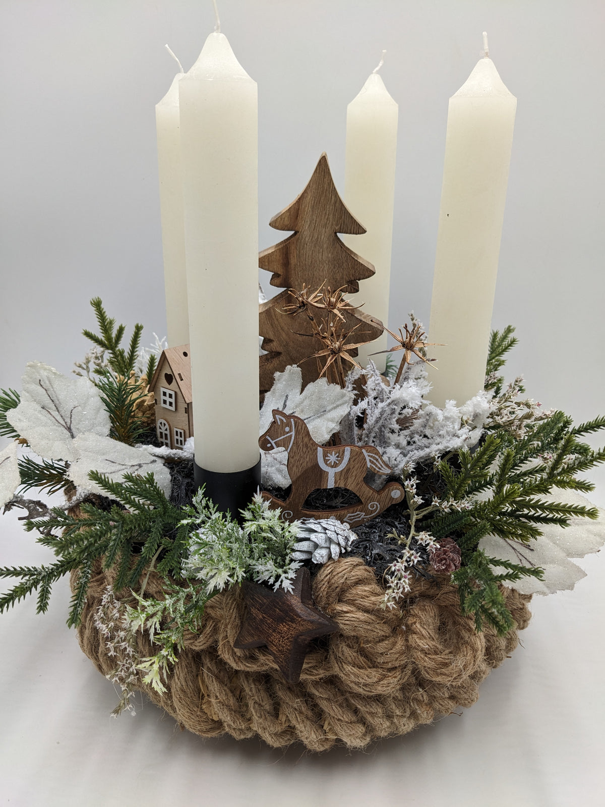 Adventsgesteck in Seilschale mit vier cremefarbenen Kerzen, Holztanne, Holzhaus und Schaukelpferd