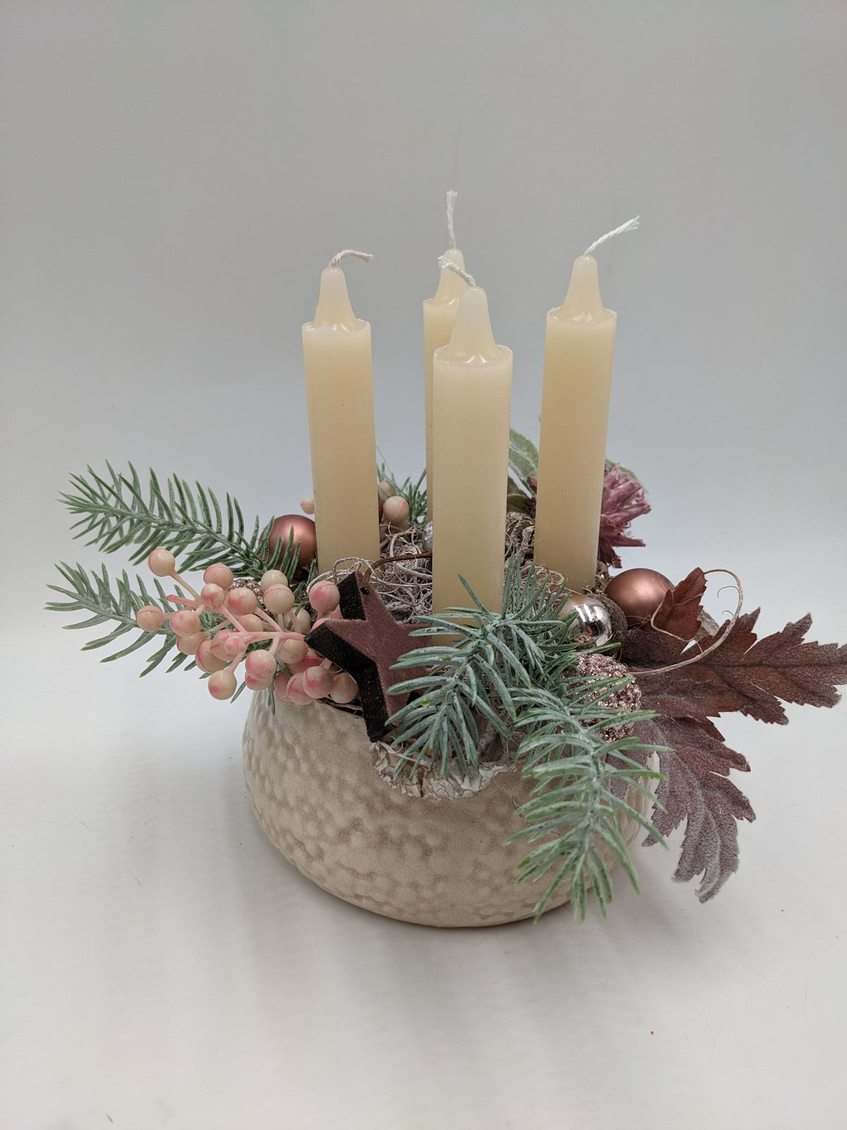 Adventsgesteck von der Seite: Kerzen, roséfarbene Kugeln, Eicheln und altrosa Blätter über gehämmerter Schale