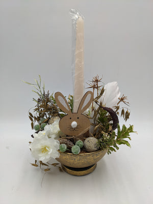 Ostergesteck in goldener Schale mit Holzhase, cremefarbener Stabkerze, weißen Blüten, Eiern und Hafergräsern