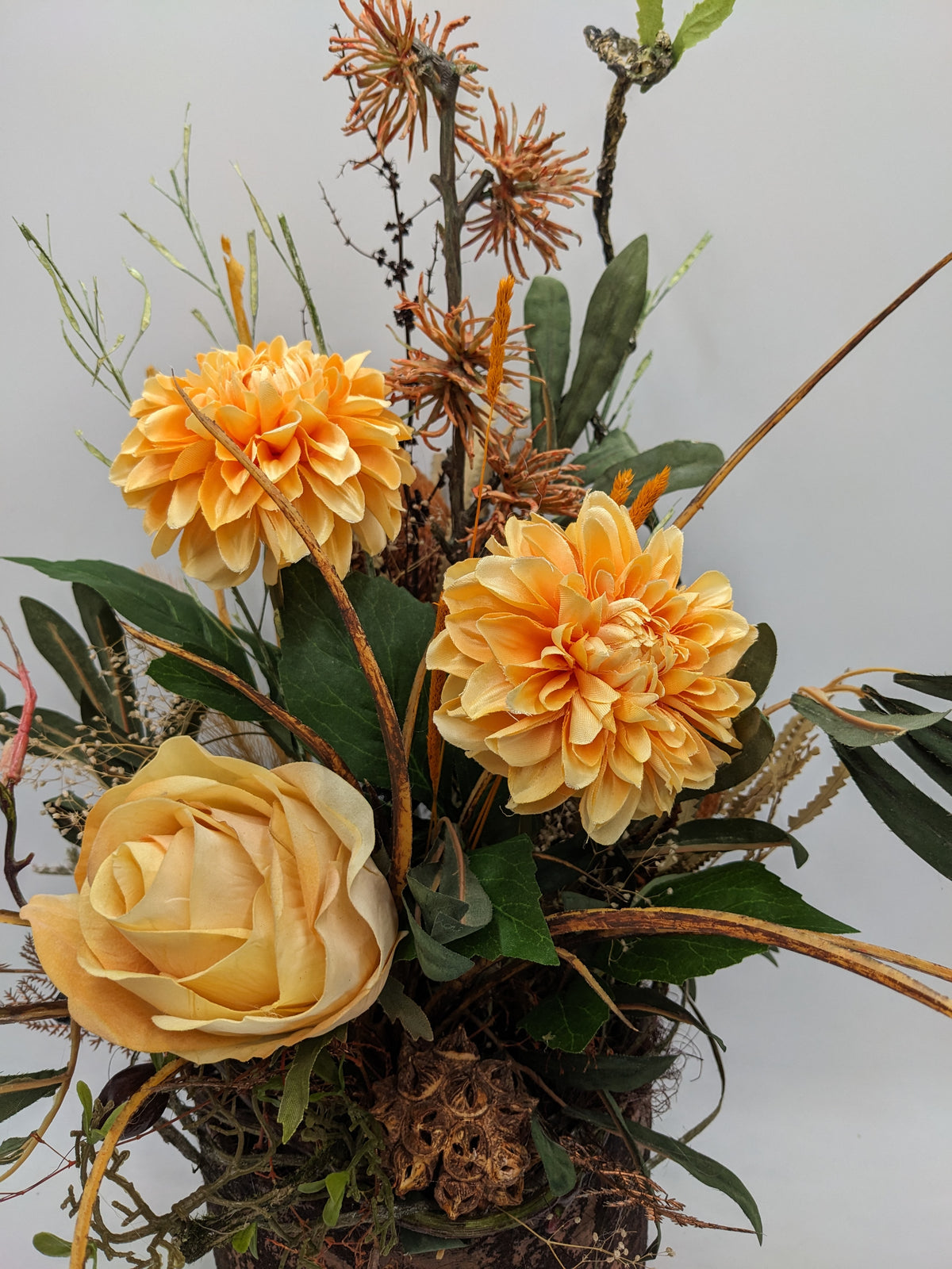 Nahaufnahme der apricotfarbenen Rose und zwei orangefarbenen Chrysanthemen zwischen grünen Blättern und Gräsern