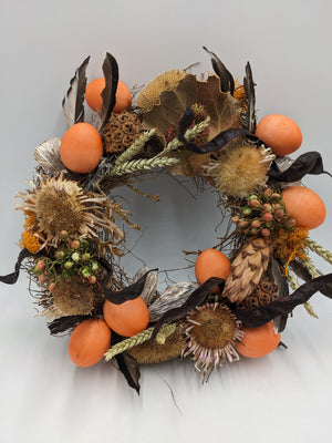 Osterkranz mit orangefarbenen Eiern, Disteln, Ähren und braunen Federn auf Zweigring, von oben fotografiert