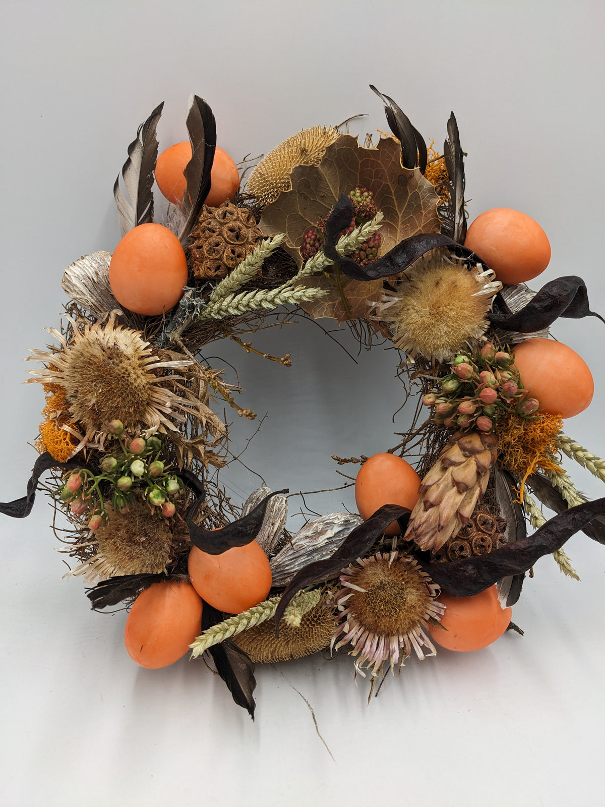 Osterkranz mit orangefarbenen Eiern, Disteln, Ähren und braunen Federn auf Zweigring, von oben fotografiert