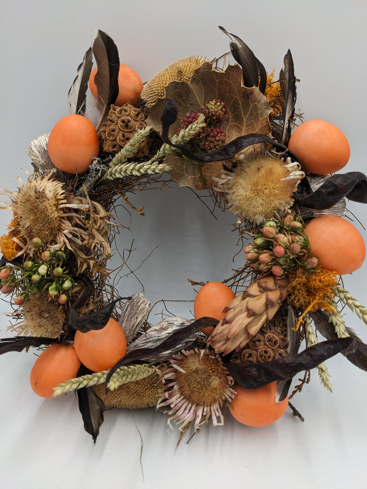 Türkranz in Orange und Natur mit Protea-Zapfen, Sonnenblumenboden, Beerenzweigen und Moos, schräg von vorn