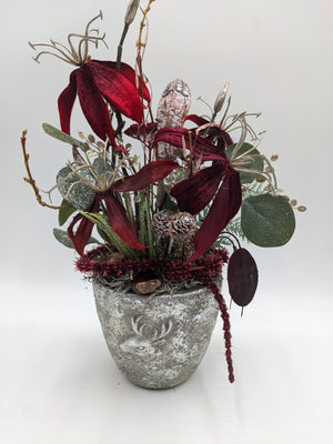 Herbstgesteck mit dunkelroten Blüten, silbernen Fruchtständen und Eukalyptus in grauem Topf mit Hirschmotiv