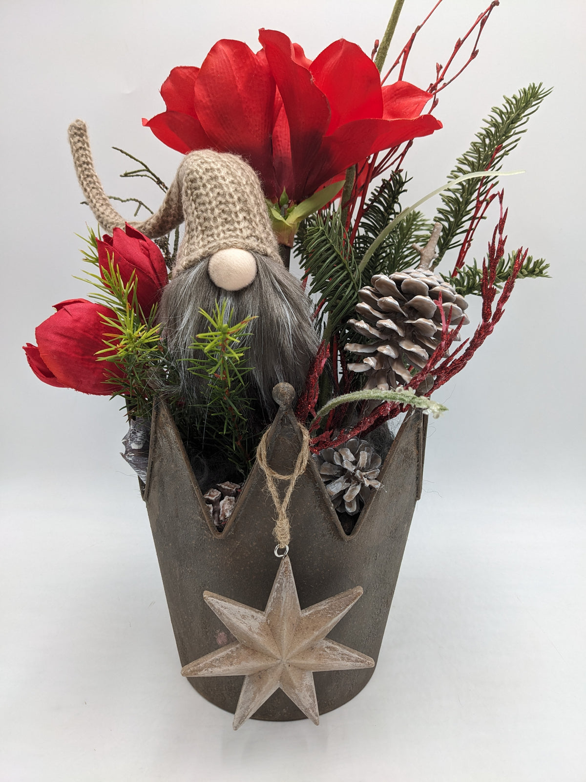 Wintergesteck mit Wichtel, roter Amaryllis, Tannenzweigen und Zapfen in grauem Metallgefäß mit Kronenrand