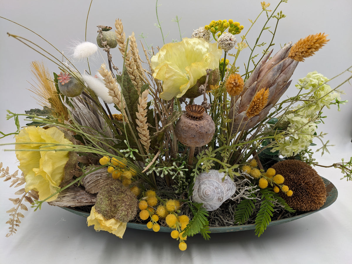 Flaches Sommergesteck in ovaler Schale mit gelben Mohnblüten, Ähren, Beerenkugeln und Schneckenhaus