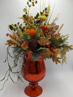 Herbstgesteck im orangefarbenen Glaspokal mit Kürbissen, Beeren, Ahornblättern und hellen Weizenähren