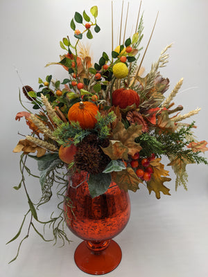 Hohes Herbstgesteck von vorn: orangefarbener Samtkürbis, gelbe Craspedia, rote Beeren und Koniferenzweige
