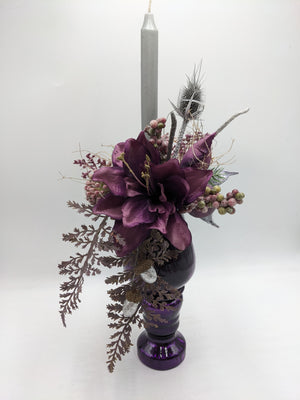Wintergesteck im lila Glaspokal mit dunkelvioletten Amaryllisblüten, silberner Stabkerze, Farn und Eicheln