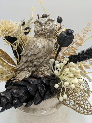 Nahaufnahme der silbernen Eulenfigur zwischen schwarzem Zapfen, weißen Beerendolden und goldenem Glitzerblatt