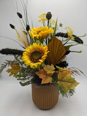 Herbstgesteck mit zwei gelben Sonnenblumen, schwarzer Mohnkapsel, Palmblatt und Laub im braunen Rillentopf