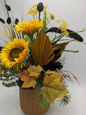 Nahaufnahme des Herbstgestecks: Sonnenblume, goldbraunes Palmblatt, schwarze Gräser und gelb-orangefarbenes Ahornlaub