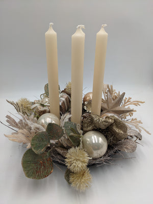 Adventsgesteck von der Seite mit drei cremefarbenen Kerzen, Geschenkpäckchen, grünen Blättern und Perlmuttkugeln