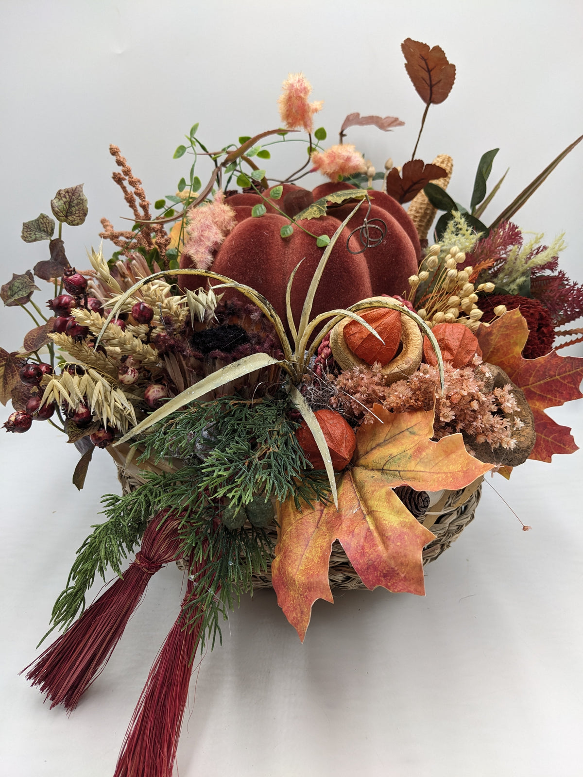 Herbstgesteck im Korb mit rostrotem Kürbis, orangefarbenen Physalis, Ahornblatt, Hagebutten und hellen Ähren