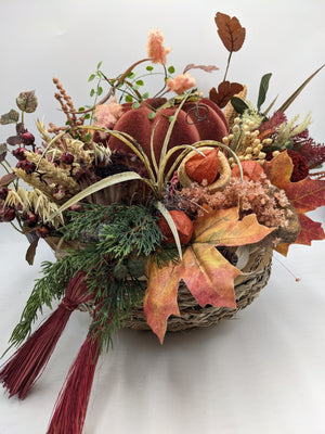Herbstgesteck von vorn: Kürbis in Rostrot, Physalis, Ahornblatt in Orange und Gelb, Gräser über dem Korbrand