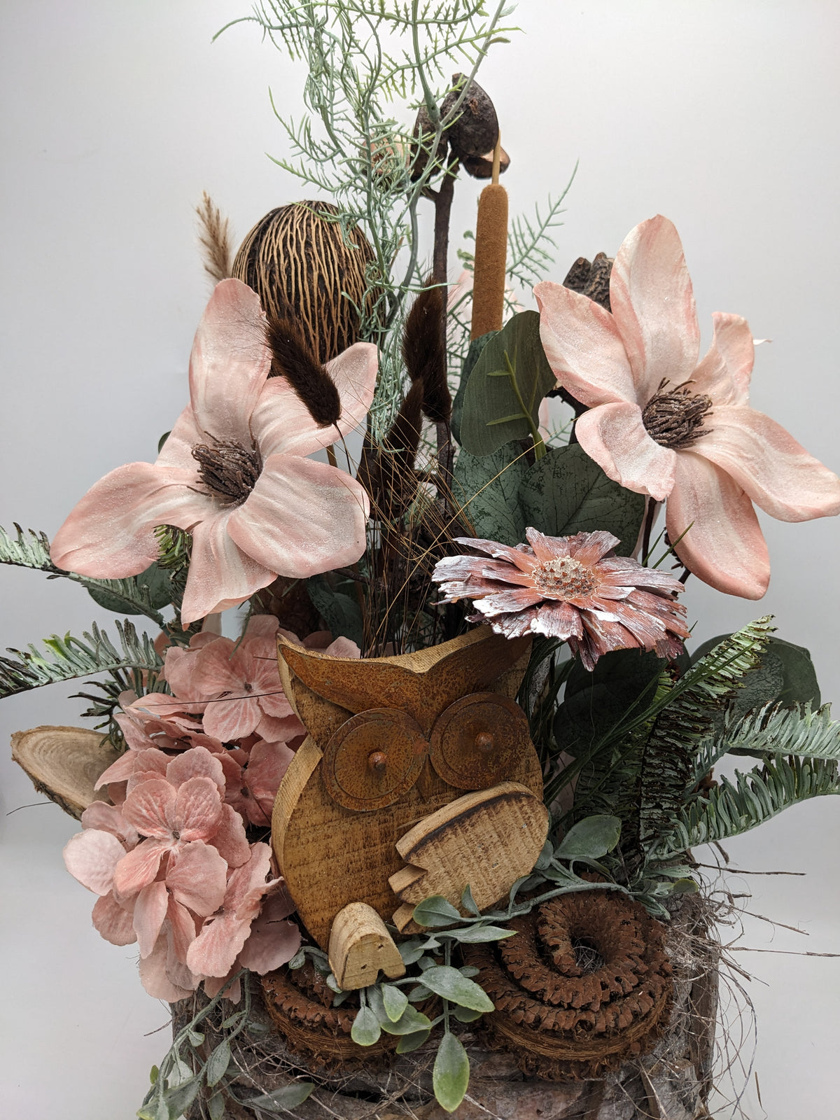 Nahaufnahme der Holzeule zwischen apricotfarbenen Magnolien, Hortensien, Rohrkolben und Farnwedeln