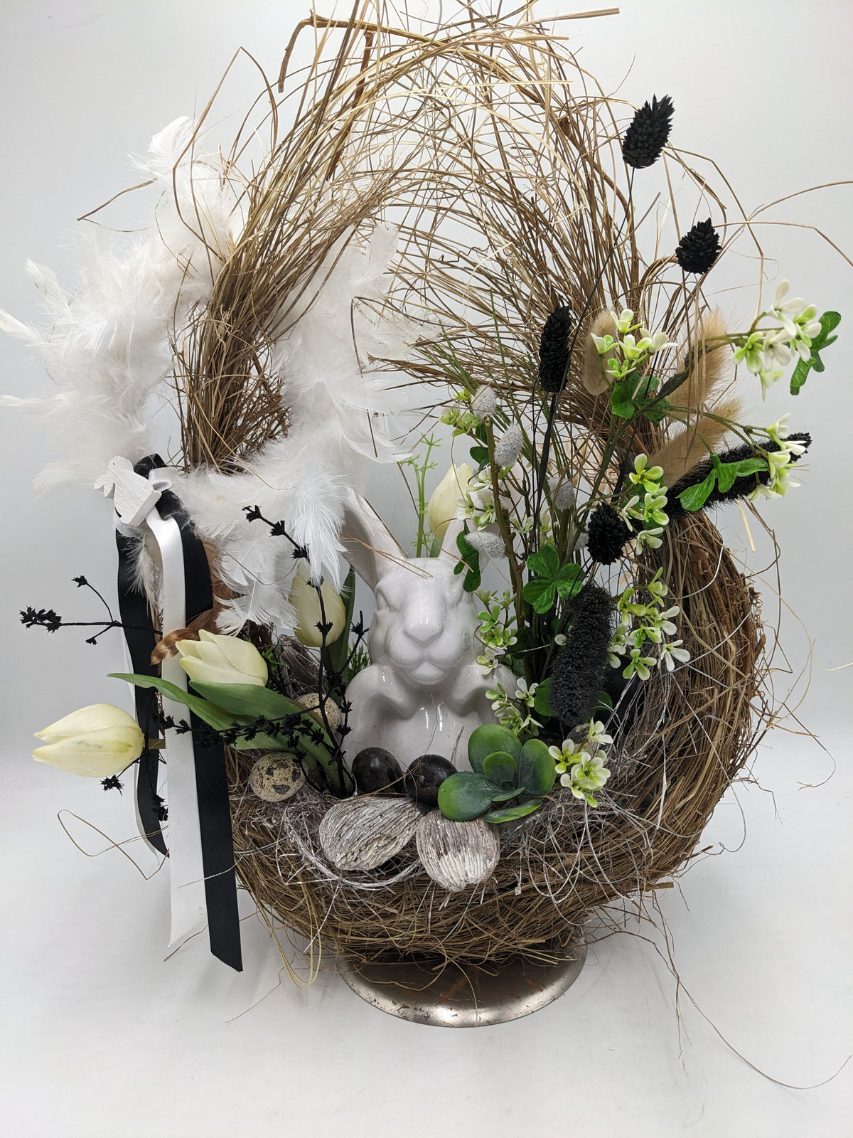 Ostergesteck im hohen Zweignest mit weißem Keramikhasen, cremefarbenen Tulpen, Federn und schwarz-weißer Schleife