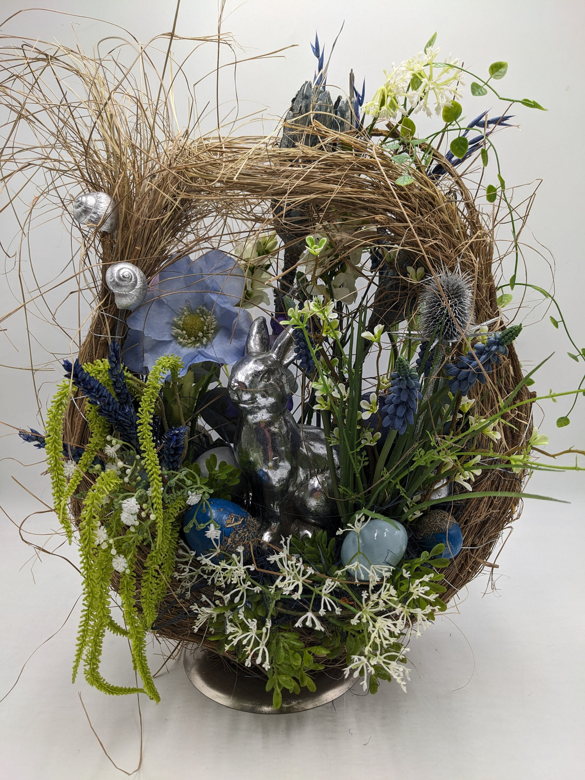 Ostergesteck im Zweigkranz mit silbernem Hasen, blauen Ostereiern, Hyazinthen und Gräsern auf Metallfuß