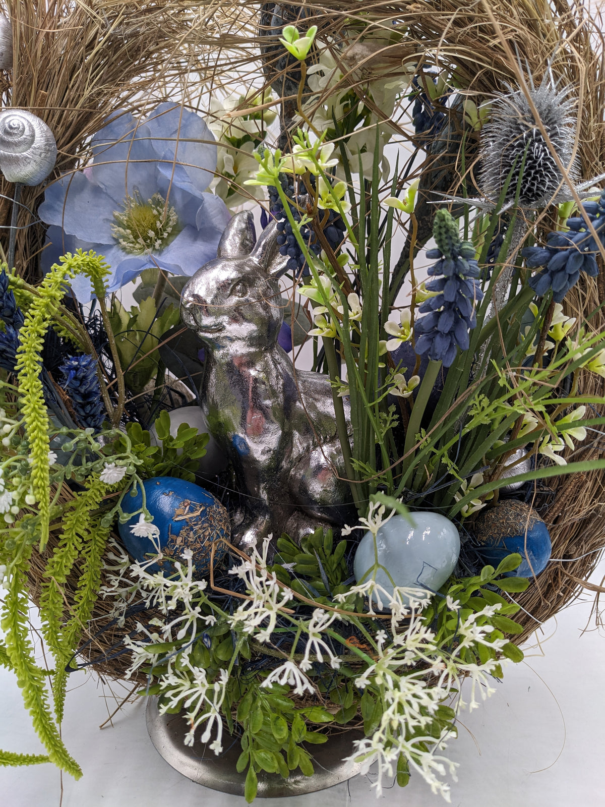 Nahaufnahme: silberner Hase zwischen blauen und hellblauen Ostereiern, Traubenhyazinthen und weißen Blüten