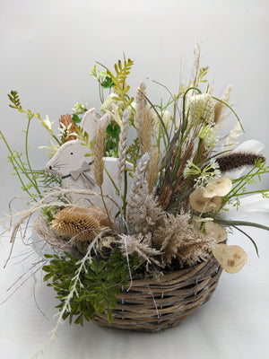 Ostergesteck im Weidenkorb mit Holzhase, Nest mit Eiern, Schachbrettblumen, Ähren und hellen Gräsern