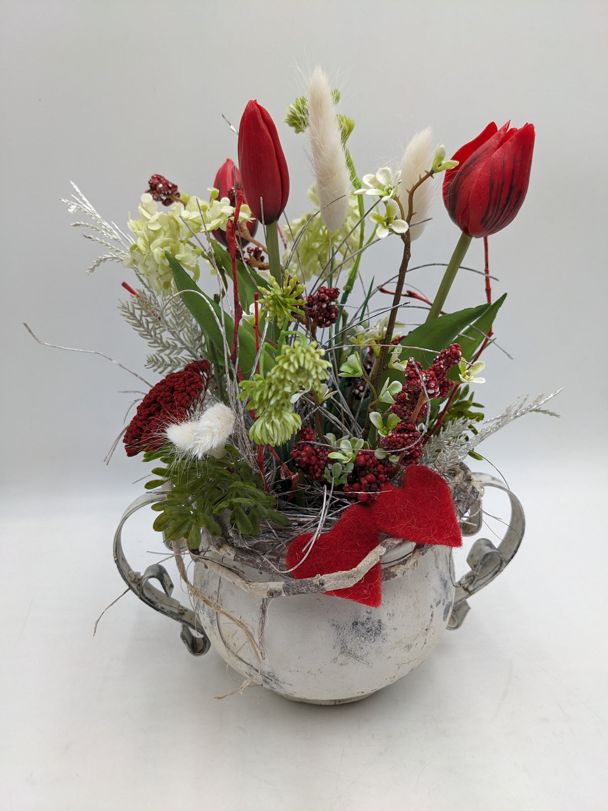 Frühlingsgesteck mit roten Tulpen, weißen Federgräsern und roten Beeren in weißem Kännchen mit Filzherz