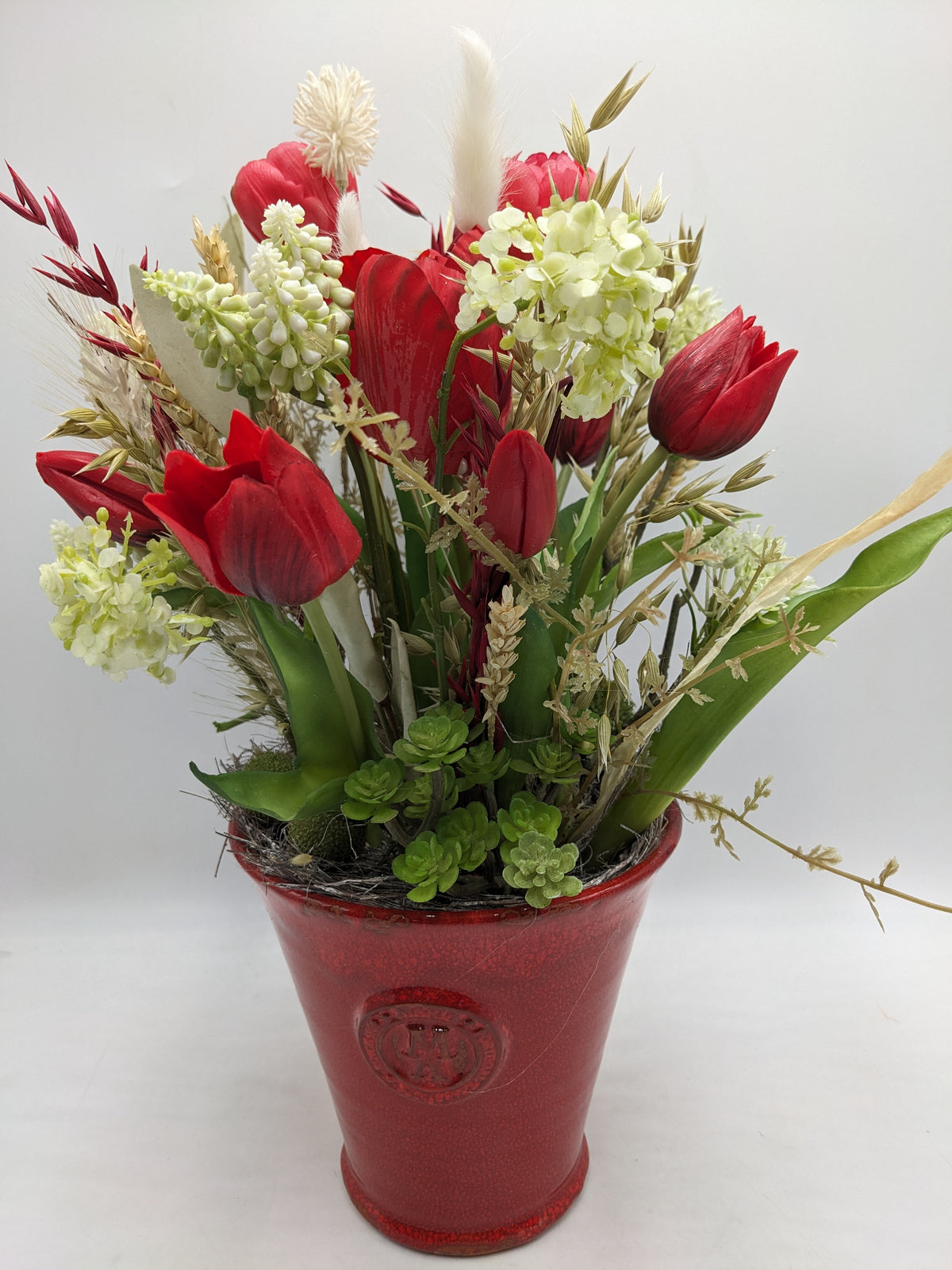 Frühlingsgesteck mit roten Tulpen, weißen Hyazinthen und Trockengräsern in rotem Keramiktopf mit Wappenrelief