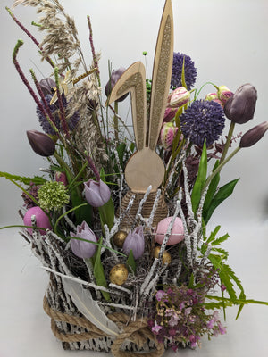 Ostergesteck von vorn: Tulpen, Schachbrettblumen, goldene Eier, weiße Feder und Gräser im Korb