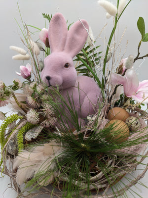 Nahaufnahme des Ostergestecks: rosa Hase zwischen Gräsern, daneben zwei braune Eier und ein Wachtelei im Nest
