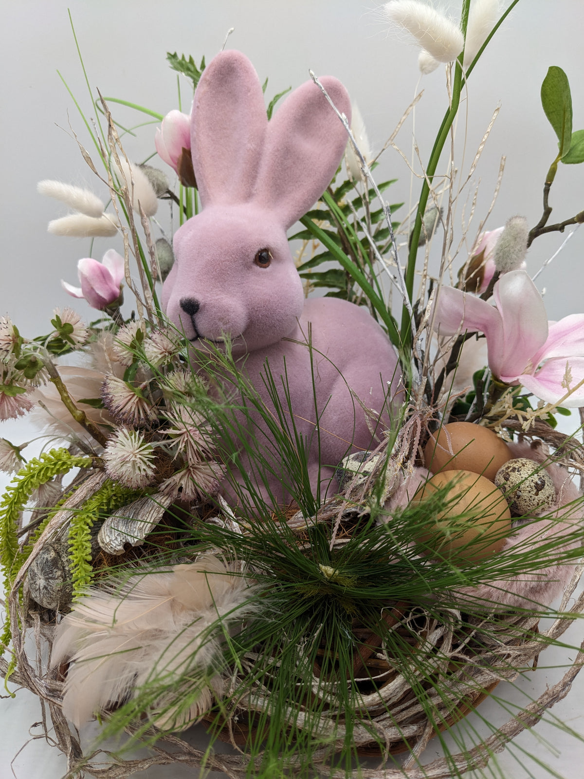 Nahaufnahme des Ostergestecks: rosa Hase zwischen Gräsern, daneben zwei braune Eier und ein Wachtelei im Nest