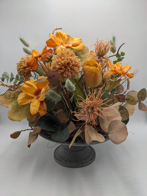 Gesteck in Orange mit Tulpe, Spider-Blüten, Chrysanthemen und Eukalyptusblättern auf grauem Metallfuß