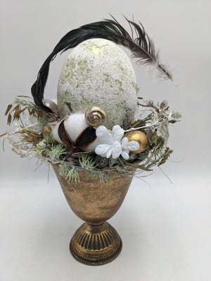 Ostergesteck aus der Nähe: weiße Blüte, goldene Wachteleier, Ähren und grüne Zweige im goldenen Pokal