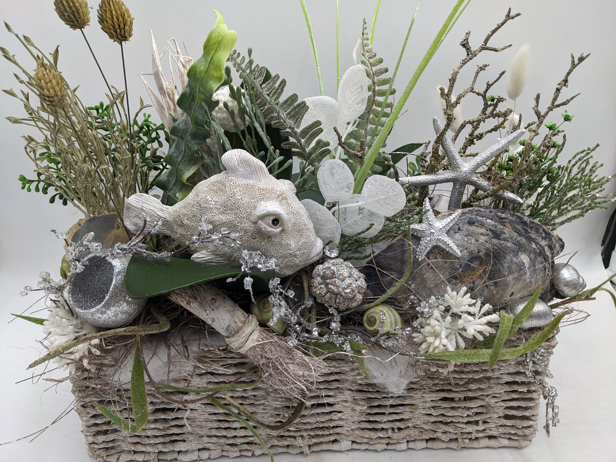 Nahansicht des Gestecks: Fisch, Austernschale, weiße Koralle, Schneckenhäuser und glitzernde Zweige im Weidenkorb