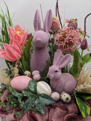 Nahaufnahme der beiden geflockten Hasen zwischen rosa Tulpen, Alliumdolde und gesprenkelten Wachteleiern