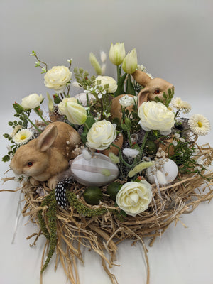 Osterkranz von oben: zwei Hasenfiguren im Strohnest mit weißen Rosen, grün-weißen Tulpen, grünen Eiern und Gräsern