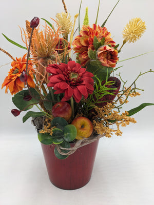 Herbstgesteck im roten Topf mit roter Gerbera, orangen Dahlien, Spider-Blüten, Äpfeln und Gräsern