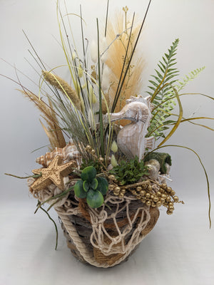 Maritimes Sommergesteck im Korb mit Seepferdchen, Gräsern, Farn, Seestern und Muschel in Creme und Gold