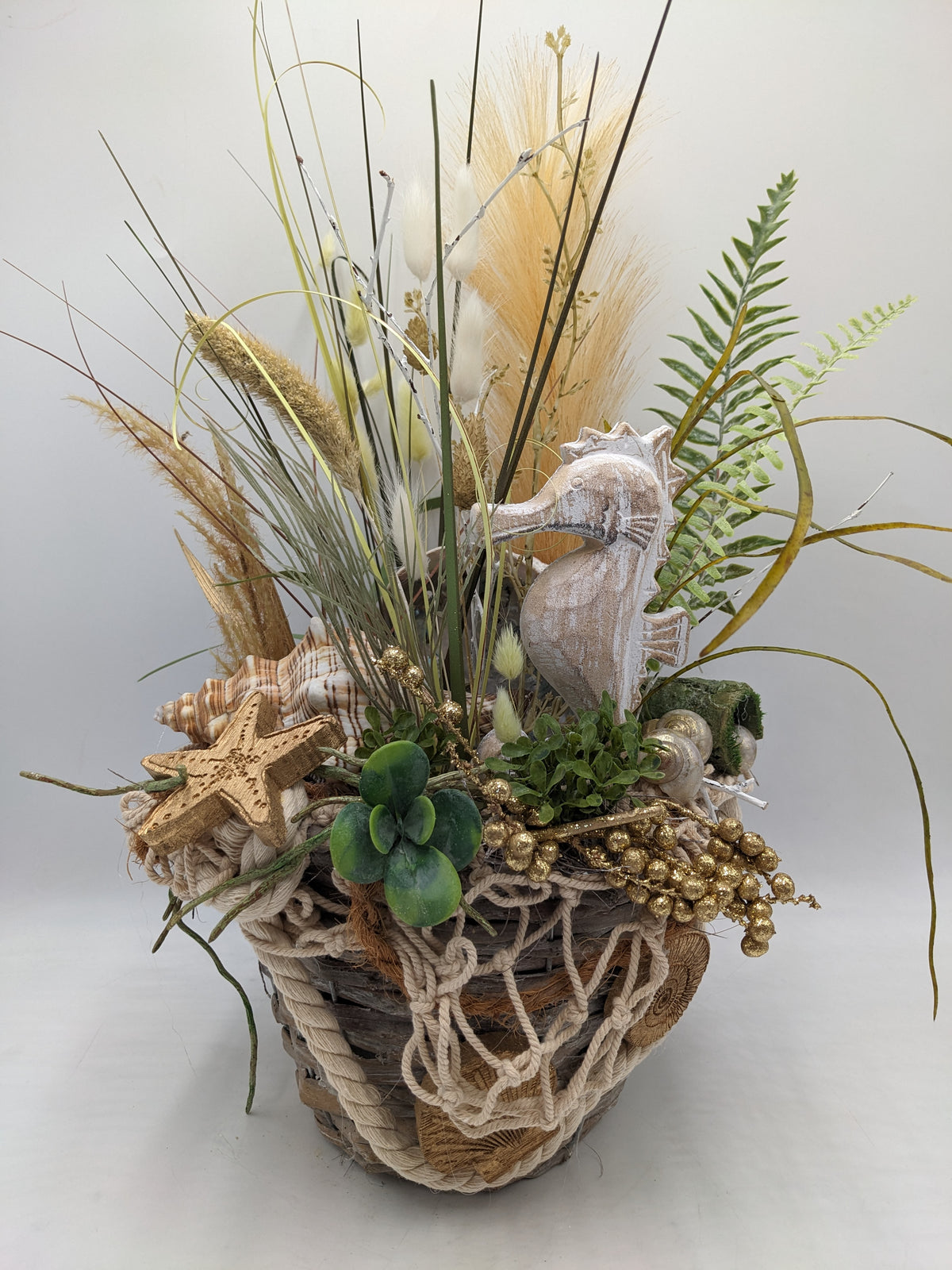 Maritimes Sommergesteck im Korb mit Seepferdchen, Gräsern, Farn, Seestern und Muschel in Creme und Gold
