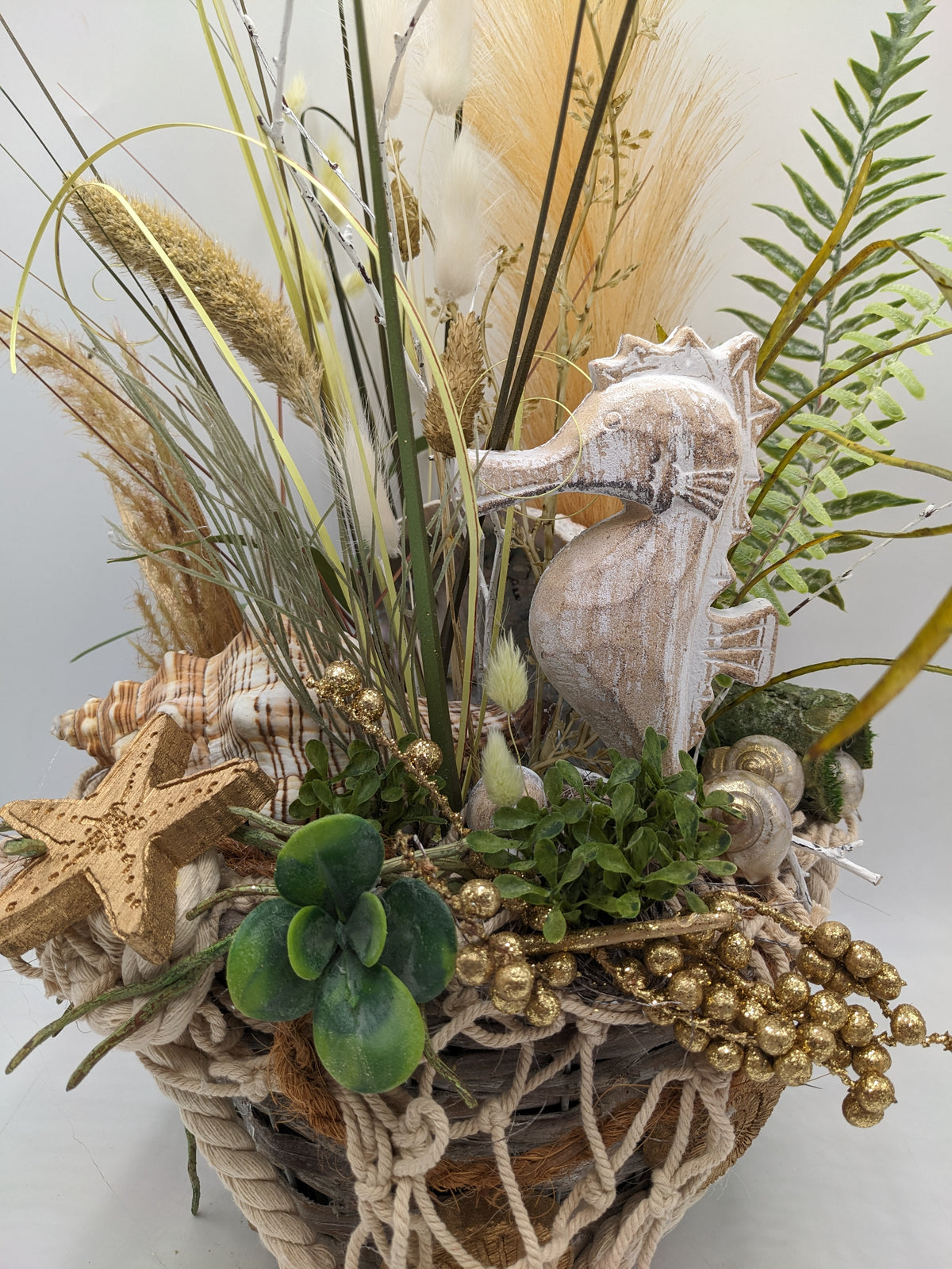 Detail des Sommergestecks: weiß gekalktes Seepferdchen, goldener Seestern, Sukkulente und goldene Beeren