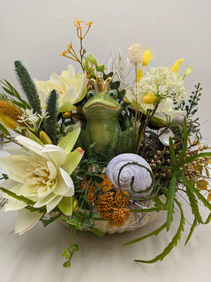 Tischgesteck mit Frosch mit goldener Krone, weißem Schneckenhaus, Lilie, weißen Dolden und goldenen Beerenzweigen