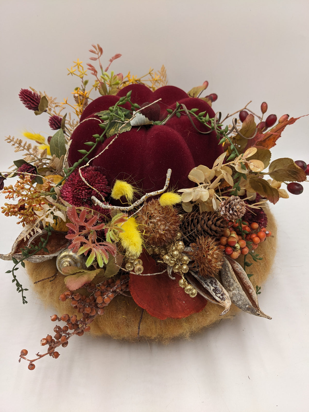 Herbstgesteck von vorn: roter Kürbis, orangefarbene Beerenrispen, Samenkapseln, Schnecke und goldene Beeren