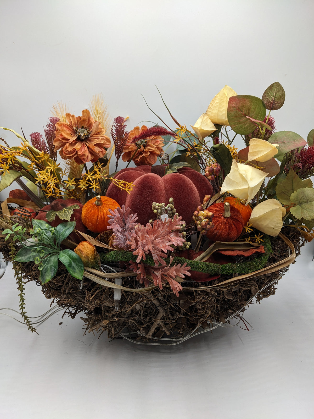 Großes Herbstgesteck in Geästschale mit bordeauxrotem Samtkürbis, orangefarbenen Blüten, Physalis und Gräsern