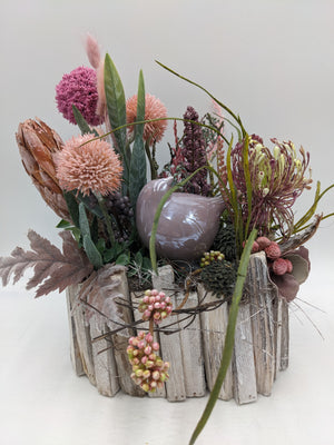 Sommergesteck im Holztopf mit rosa Kugelblüten, Protea, Spider-Blüte und altrosa Keramikvogel