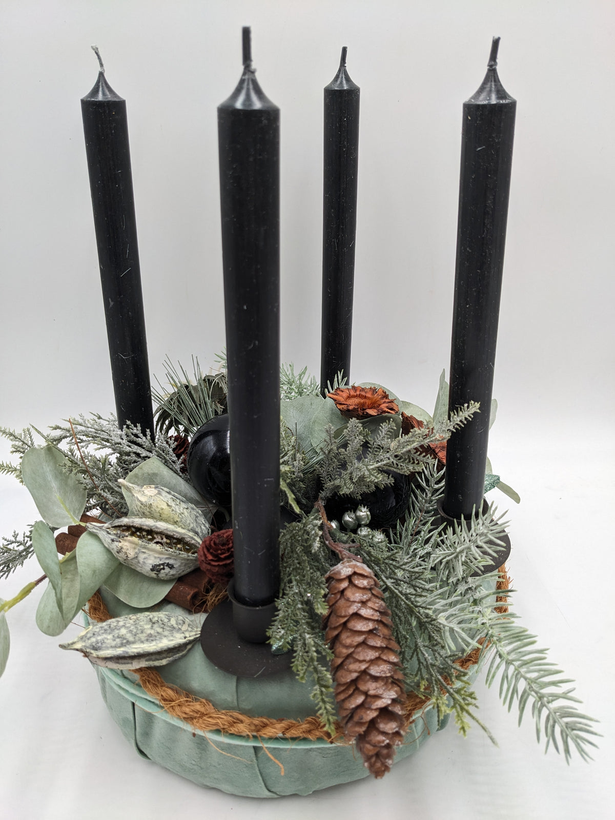 Adventskranz von schräg oben: schwarze Kugeln, Zimtstangen, Samenkapseln und rostrote Blüten zwischen frostigen Zweigen