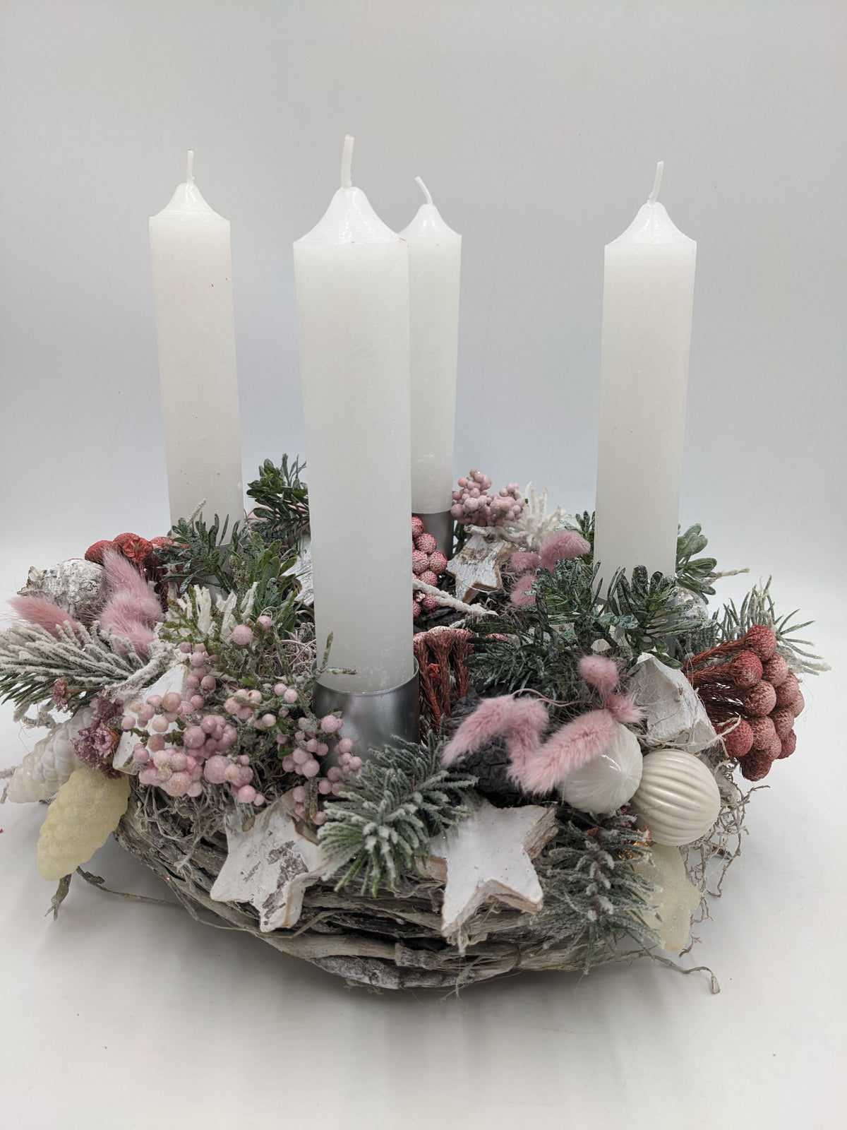 Adventskranz in Rosa und Weiß mit vier hohen weißen Stabkerzen, rosa Beeren, Zapfen und beschneiter Tanne