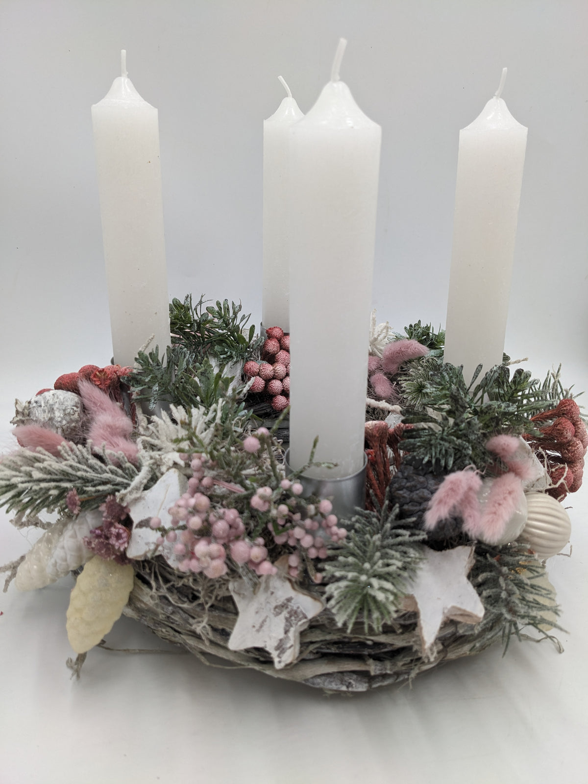 Adventskranz von vorn: weiße Kerzen, Birkenrinde-Sterne, helle Kugeln und rosa Gräser auf hellem Geflecht