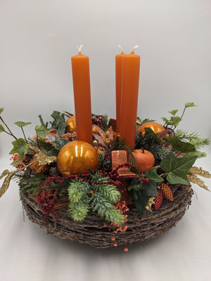 Adventskranz mit vier orangefarbenen Stabkerzen, goldenen Kugeln, Efeu und rotem Beerenzweig auf Rindenkranz