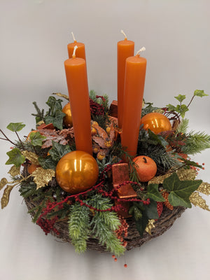 Adventskranz von schräg oben: orange Kerzen, Kupferkugel, kleiner Apfel, Zapfen und goldene Glitzerblätter