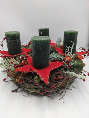 Adventskranz von der Seite: vier dunkelgrüne Stumpenkerzen auf roten Filzsternen, grüne Kugeln, Zapfen und rote Beeren