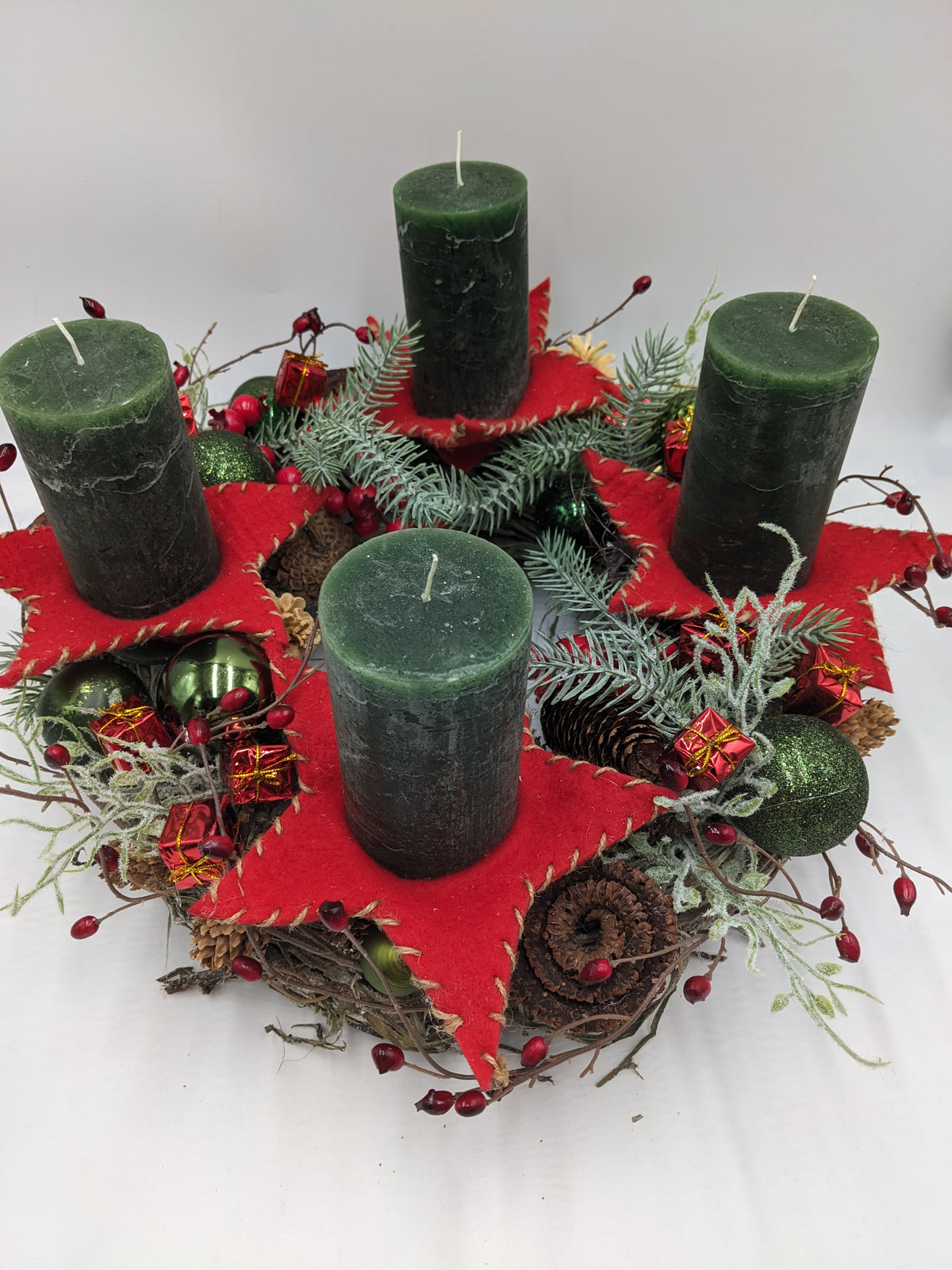 Adventskranz von oben: vier grüne Kerzen, rote Filzsterne, Tannenzweige, kleine rote Päckchen und Zapfenrosen