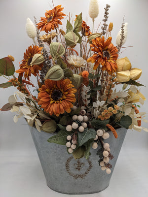 Großes Gesteck mit orangefarbenen Gerbera, grünen Physalislaternen und hellen Gräsern in grauem Zinktopf